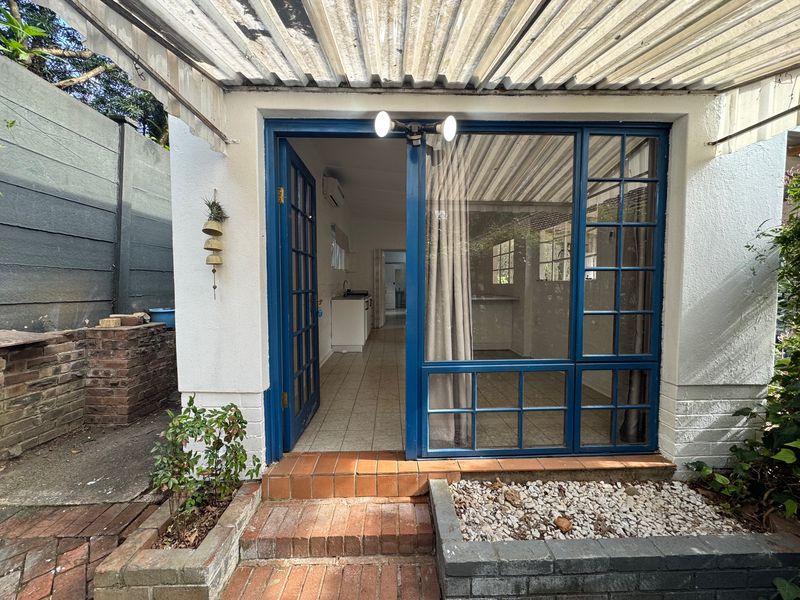 A covered patio area featuring a corrugated roof, brick steps, and blue-framed glass doors leading into the interior living space.