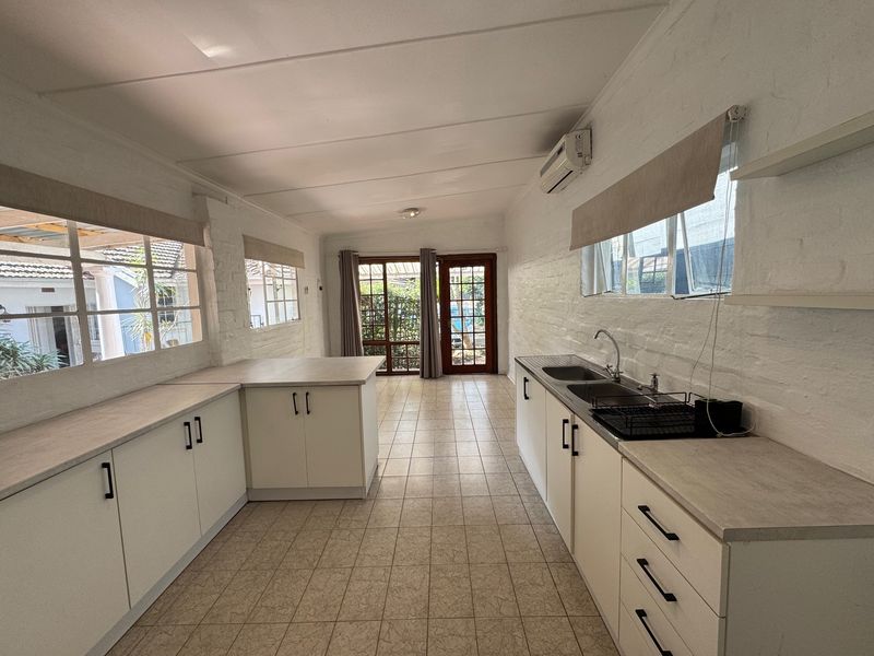 Spacious kitchen featuring ample built-in cabinetry, laminate countertops, double sink, and tiled flooring with direct access to the outdoor area.