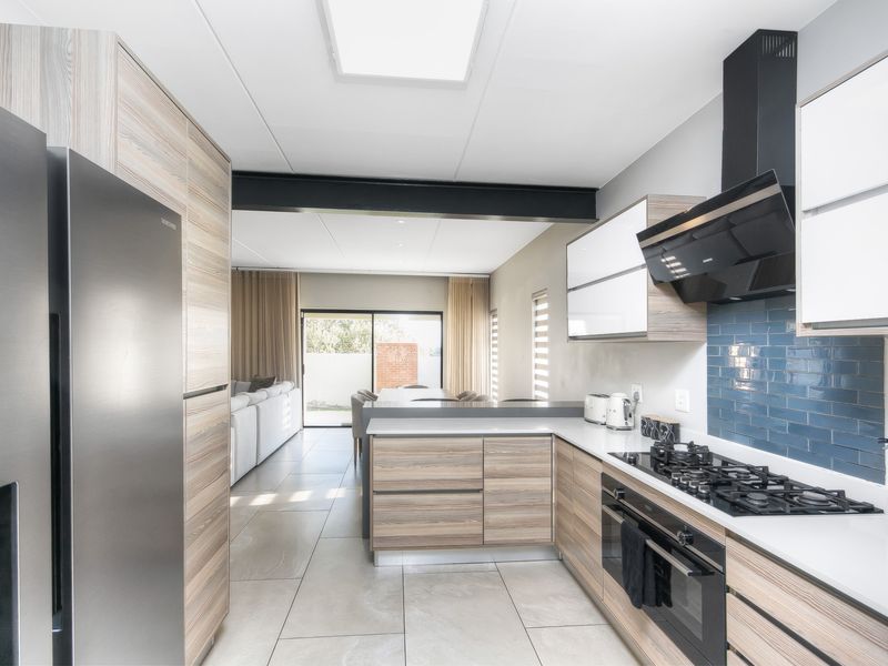 Modern open-plan kitchen featuring wood-grain cabinetry, gas hob, and sleek subway tile backsplash, flowing seamlessly into the living and dining area.