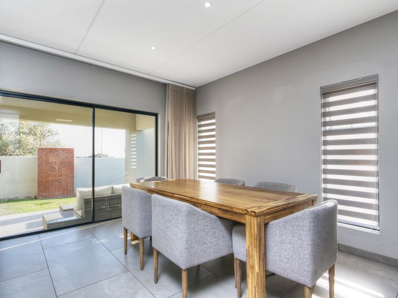A bright dining area featuring large sliding glass doors that open to a patio, tiled flooring, and modern roller blinds.