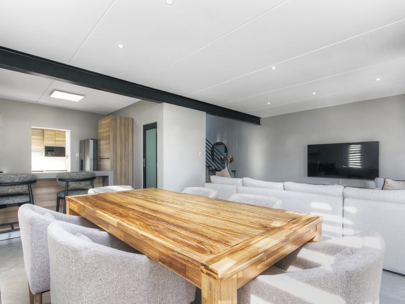 Modern open-plan living and dining area featuring a sleek kitchen with breakfast bar, recessed lighting, and an exposed structural steel beam.
