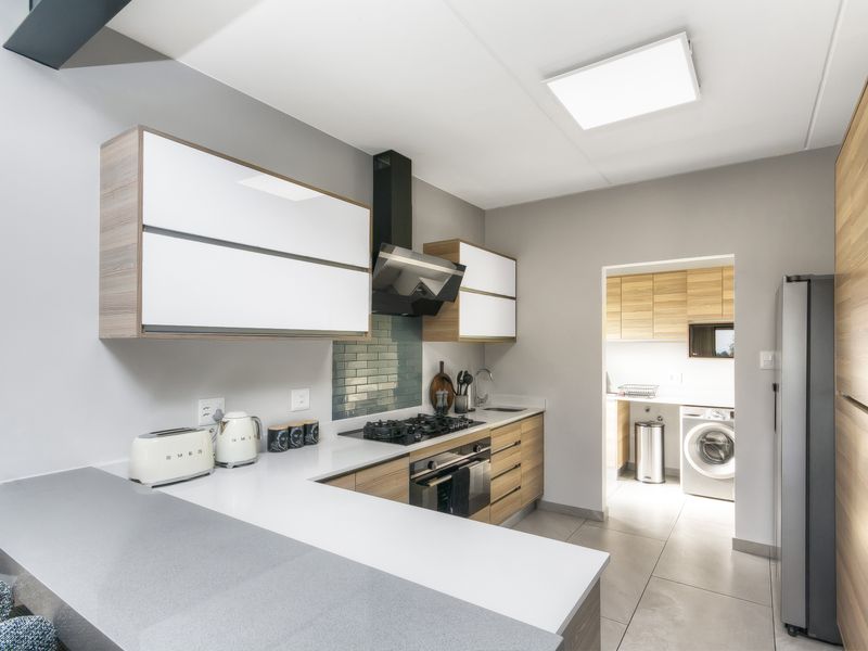 Modern kitchen featuring sleek cabinetry, stone countertops, gas hob, integrated oven, and a tiled backsplash, with an adjacent scullery area.