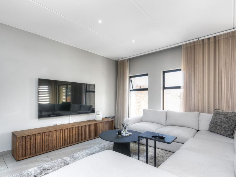Modern living room featuring tiled flooring, recessed downlights, and large windows with neutral curtains, creating a bright and contemporary atmosphere.