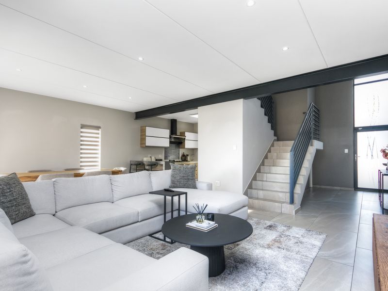 Modern open-plan living area featuring tiled floors, an exposed steel beam, a sleek staircase with metal balustrades, and a contemporary kitchen with integrated cabinetry.