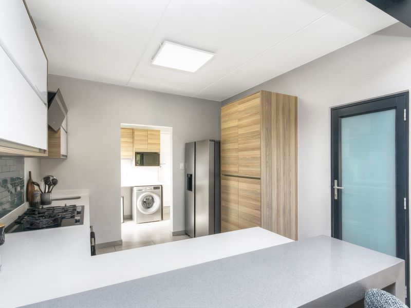 Modern kitchen featuring sleek wood-tone and white cabinetry, stone countertops, gas hob, and a convenient adjoining scullery area with laundry facilities.