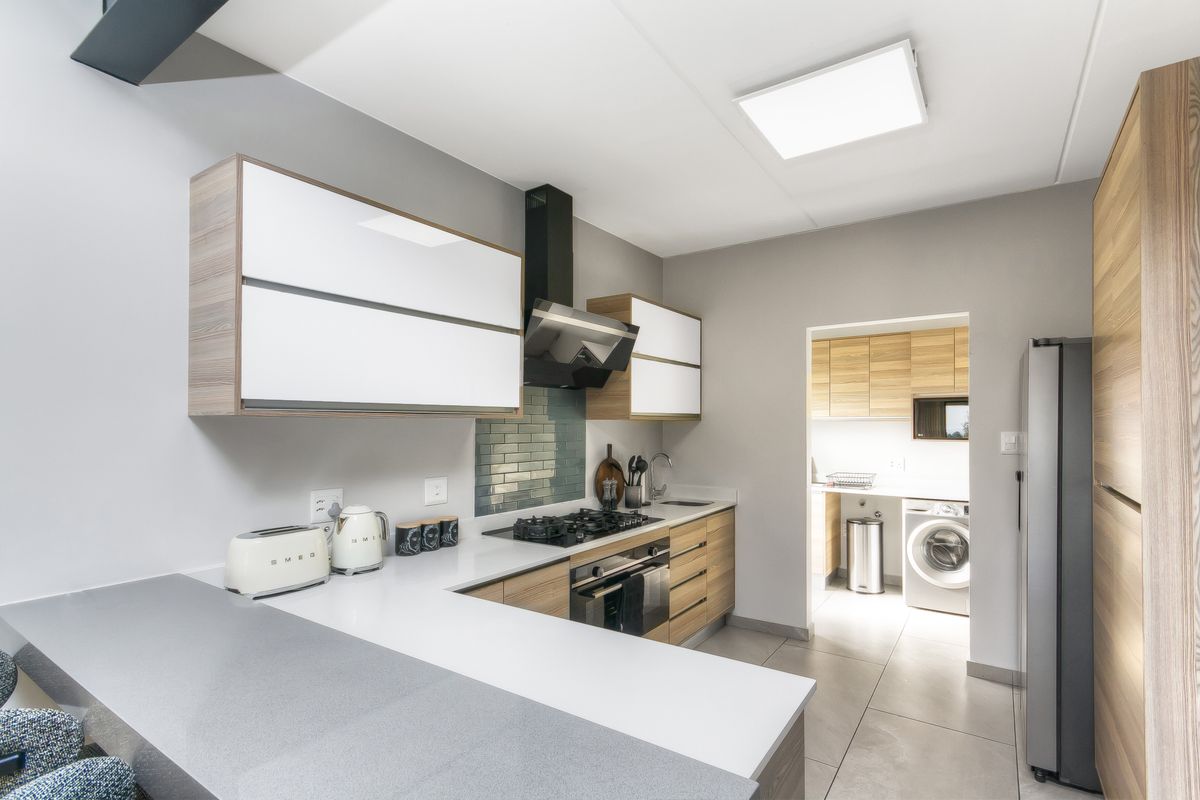 Modern kitchen featuring sleek cabinetry, stone countertops, gas hob, integrated oven, and a tiled backsplash, with an adjacent scullery area.
