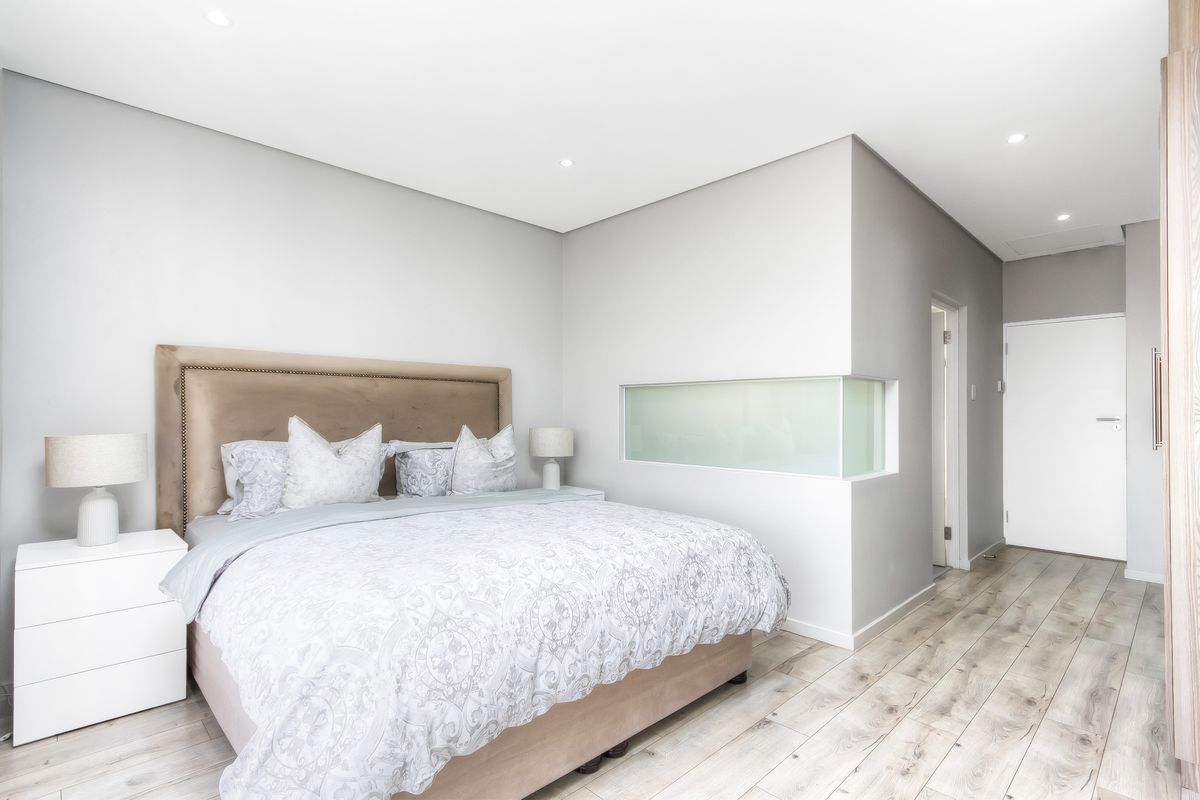 Modern bedroom featuring light laminate flooring, recessed downlighting, and a unique frosted glass feature window, creating a bright and contemporary living space.