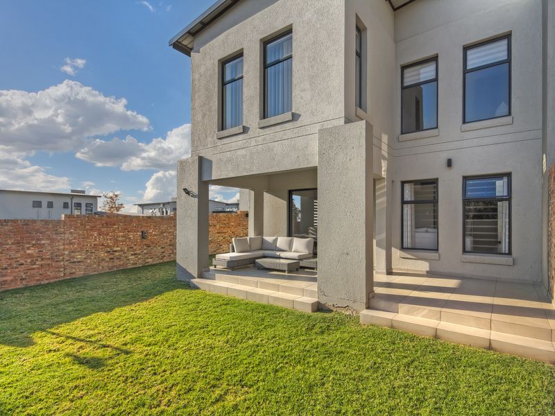 Rear view of the townhouse featuring a covered patio with tiled flooring, overlooking a private garden enclosed by a brick boundary wall.