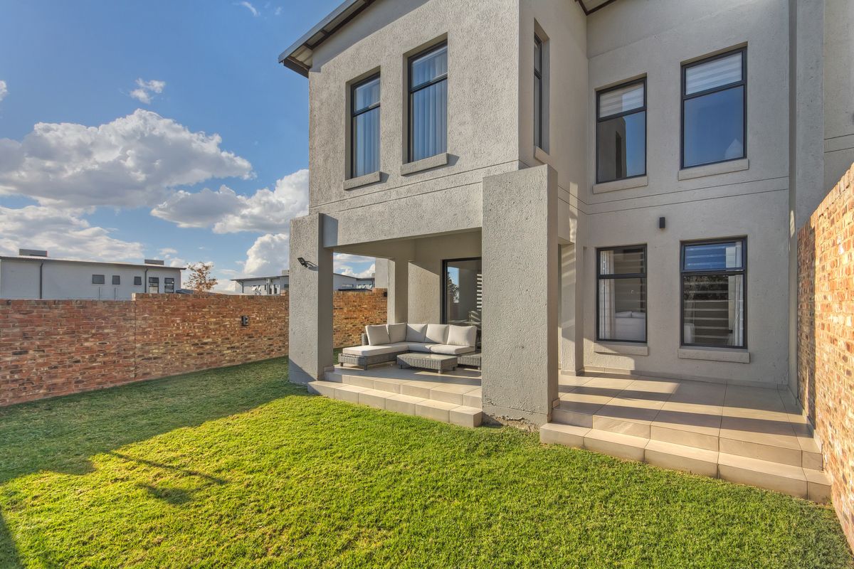 Rear view of the townhouse featuring a covered patio with tiled flooring, overlooking a private garden enclosed by a brick boundary wall.