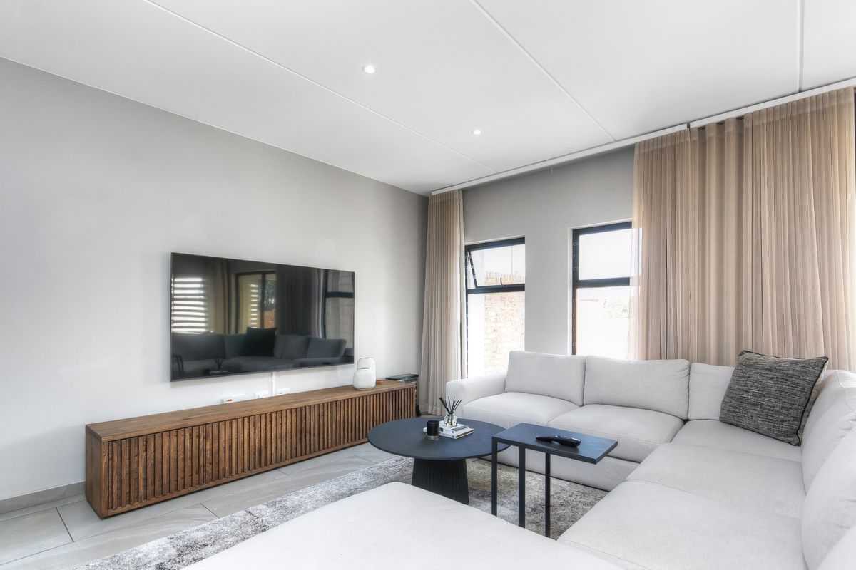 Modern living room featuring tiled flooring, recessed downlights, and large windows with neutral curtains, creating a bright and contemporary atmosphere.