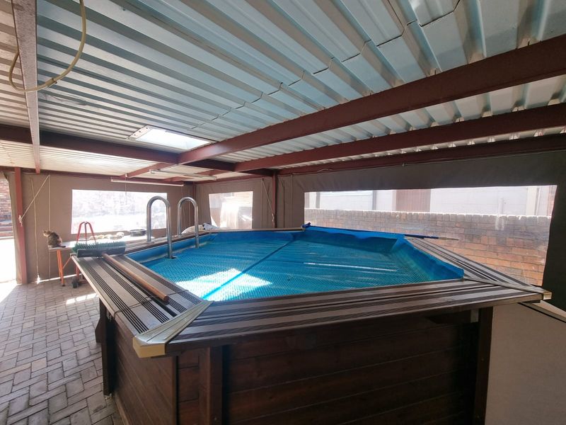 Covered outdoor area featuring an above-ground pool with timber decking, protected by a metal roof structure and brick perimeter walls.