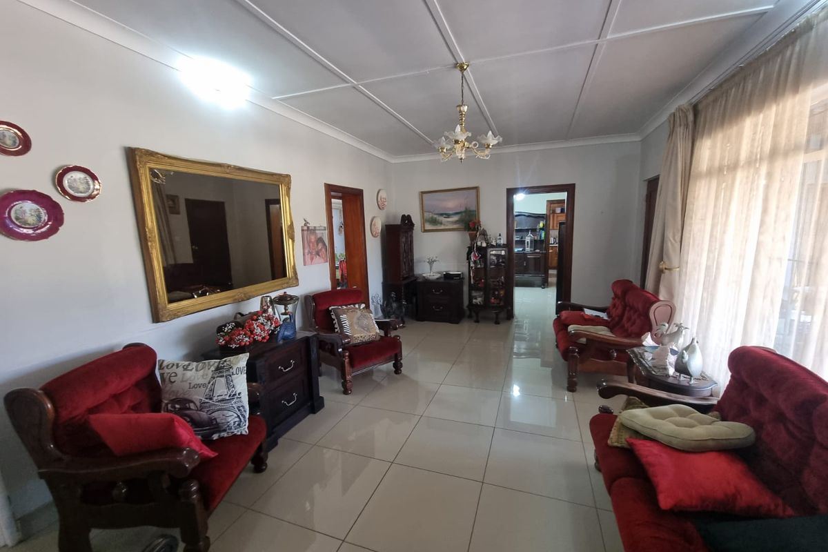 A spacious living room featuring polished floor tiles, coved ceilings, and a central chandelier, providing a functional and well-maintained living space.