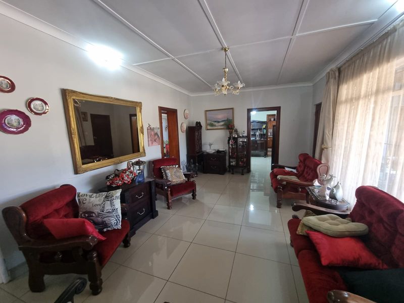 A spacious living room featuring polished floor tiles, coved ceilings, and a central chandelier, providing a functional and well-maintained living space.