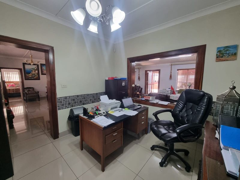 A functional home office space featuring tiled flooring, decorative coving, and a large internal window opening connecting to the adjacent living area.