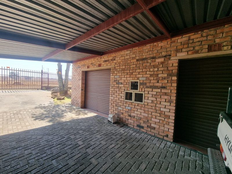 A covered carport area featuring facebrick walls, durable paved flooring, and secure roller shutter garage access.