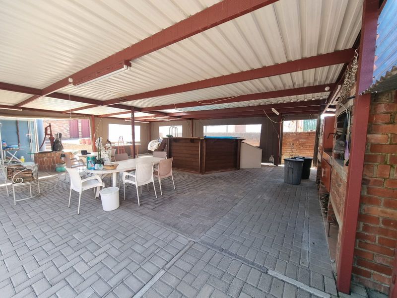 Spacious covered patio featuring a built-in braai and bar area, ideal for outdoor entertaining with durable paved flooring.