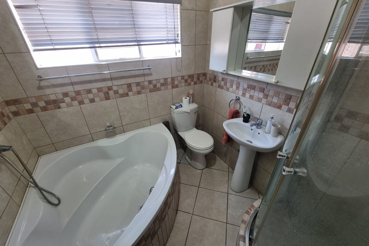 A functional bathroom featuring a corner bathtub, separate shower enclosure, pedestal sink, and tiled finishes throughout.