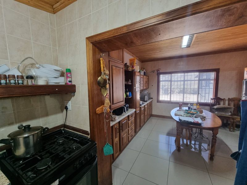 A functional kitchen featuring wooden cabinetry, tiled flooring, and a gas stove, with an adjoining dining area and timber-clad ceiling.
