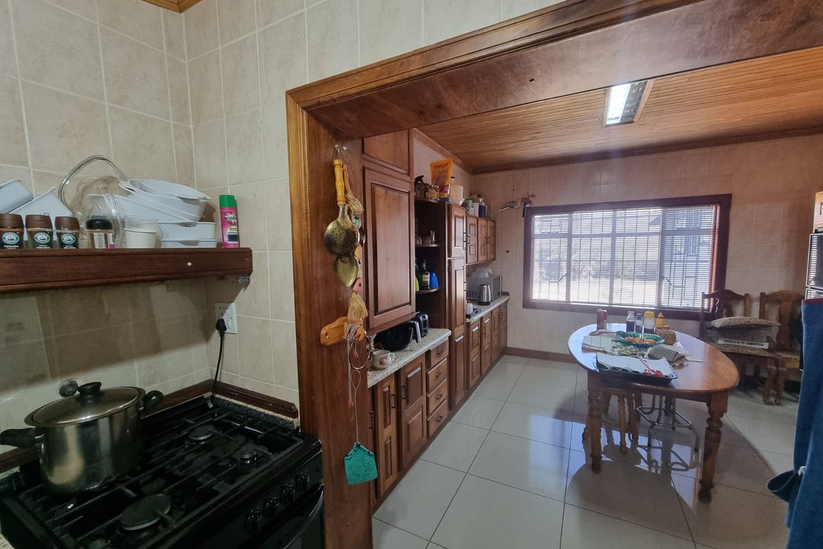 A functional kitchen featuring wooden cabinetry, tiled flooring, and a gas stove, with an adjoining dining area and timber-clad ceiling.