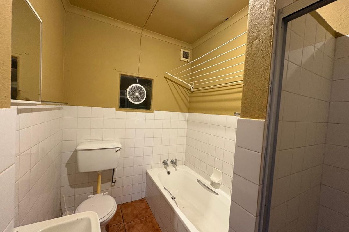 A dated bathroom featuring a standard bathtub, toilet, and wall-mounted drying rack, with tiled splashbacks and terracotta-style floor tiles.