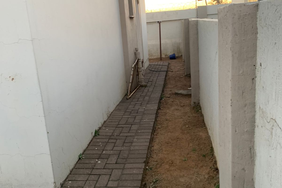 A narrow side passage of the townhouse featuring paved walkway and perimeter boundary walls.