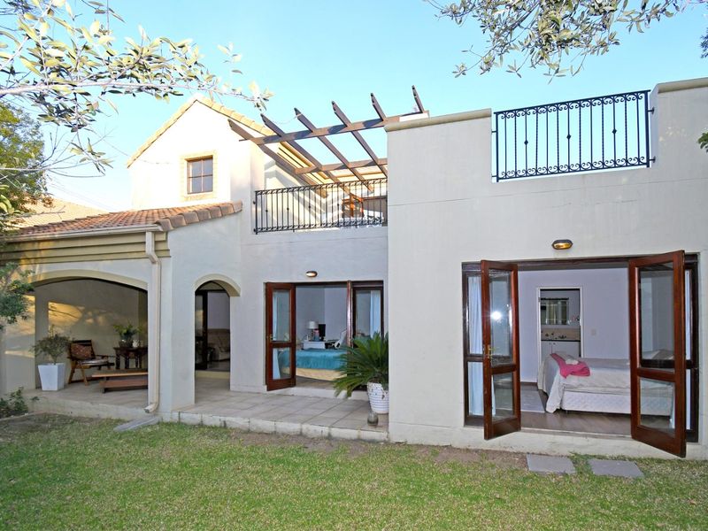 Rear view of the townhouse featuring a covered patio, upper-level balcony with wrought iron railings, and direct access to the garden through french doors.