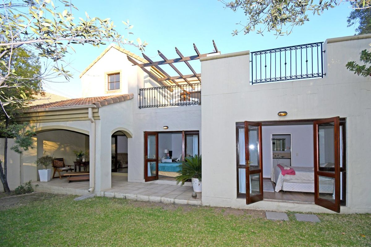 Rear view of the townhouse featuring a covered patio, upper-level balcony with wrought iron railings, and direct access to the garden through french doors.