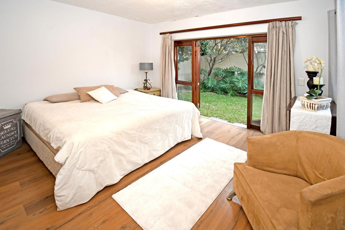 Spacious bedroom featuring warm wood-look flooring and direct access to a private garden through large sliding glass doors.