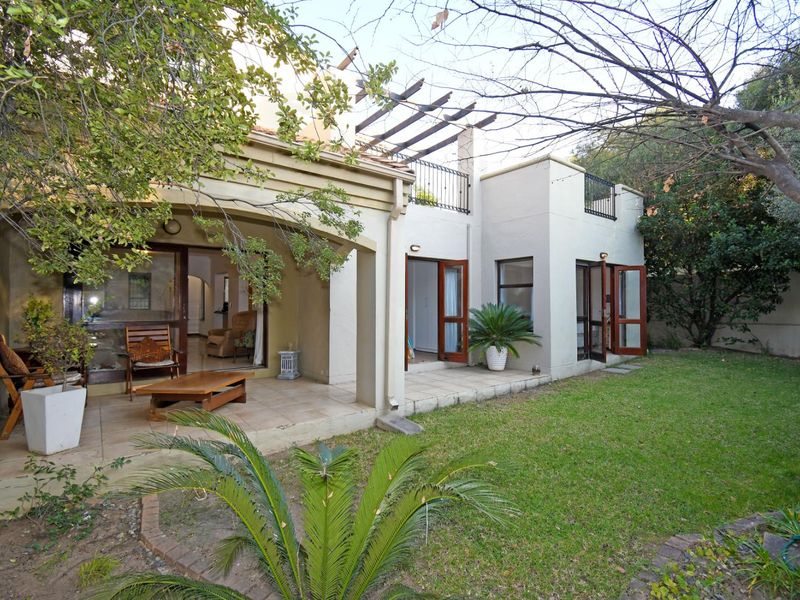 Rear view of the townhouse featuring a covered patio, a small balcony with wrought iron railings, and access to a private garden area.