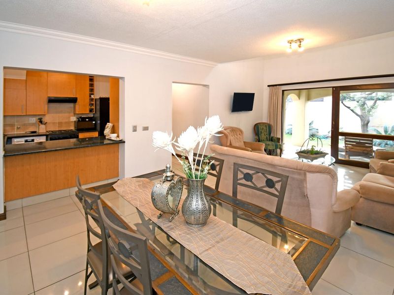 Open-plan living and dining area featuring tiled floors, coved cornicing, and a functional kitchen with granite countertops and wooden cabinetry, leading to a patio.
