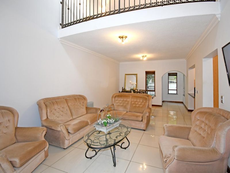 Spacious living area featuring tiled flooring, a double-volume ceiling with a wrought iron mezzanine balustrade, and an open-plan layout leading to the dining area.