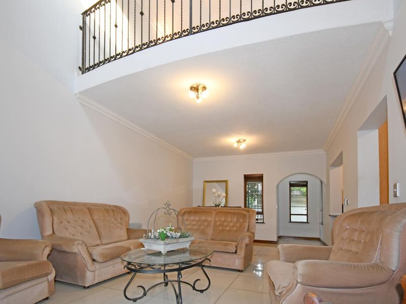 Spacious living room featuring a double-volume ceiling with a wrought iron mezzanine balcony, tiled flooring, and an elegant arched entryway.