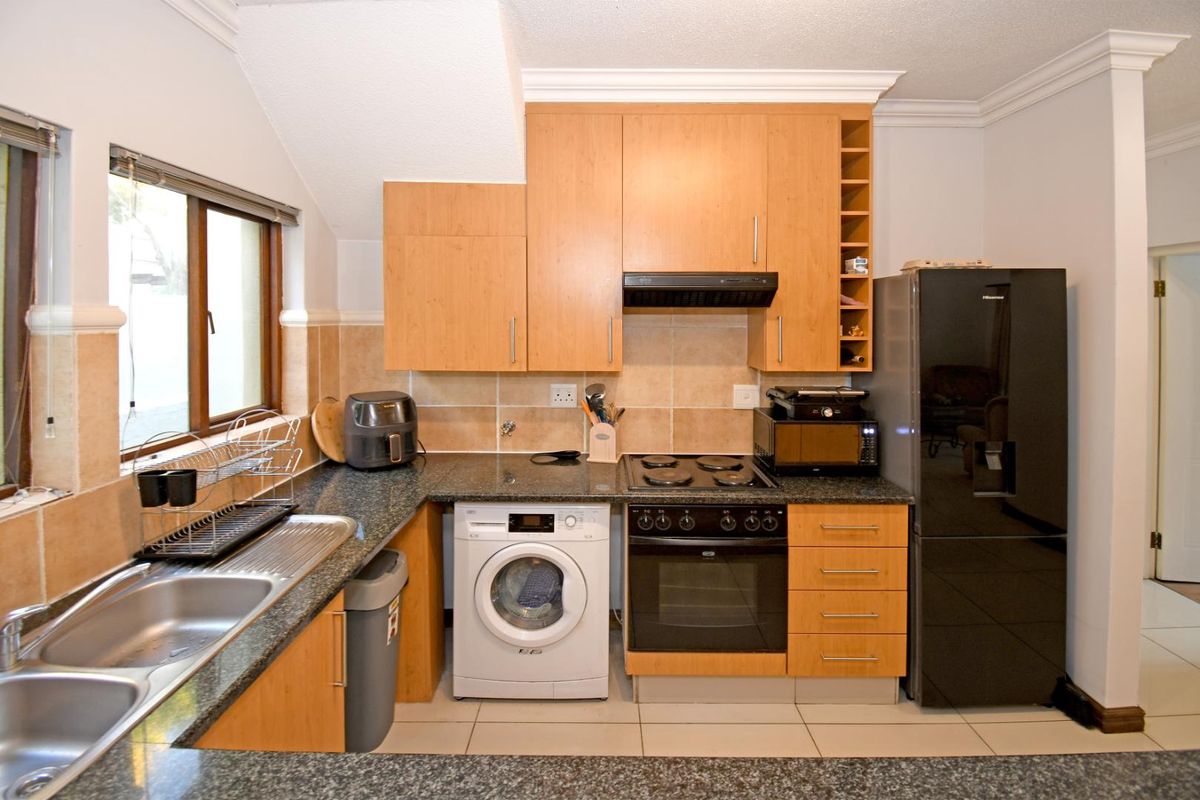 Functional kitchen featuring light wood cabinetry, granite countertops, integrated oven and hob, and tiled finishes with a dedicated space for laundry appliances.