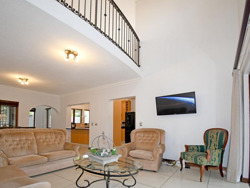 Spacious living room featuring a double-volume ceiling, wrought iron mezzanine railing, tiled flooring, and an open-plan layout connecting to the kitchen area.