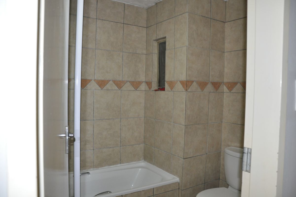 A functional bathroom featuring a built-in bathtub and toilet with neutral-toned wall tiles and a small ventilation window.