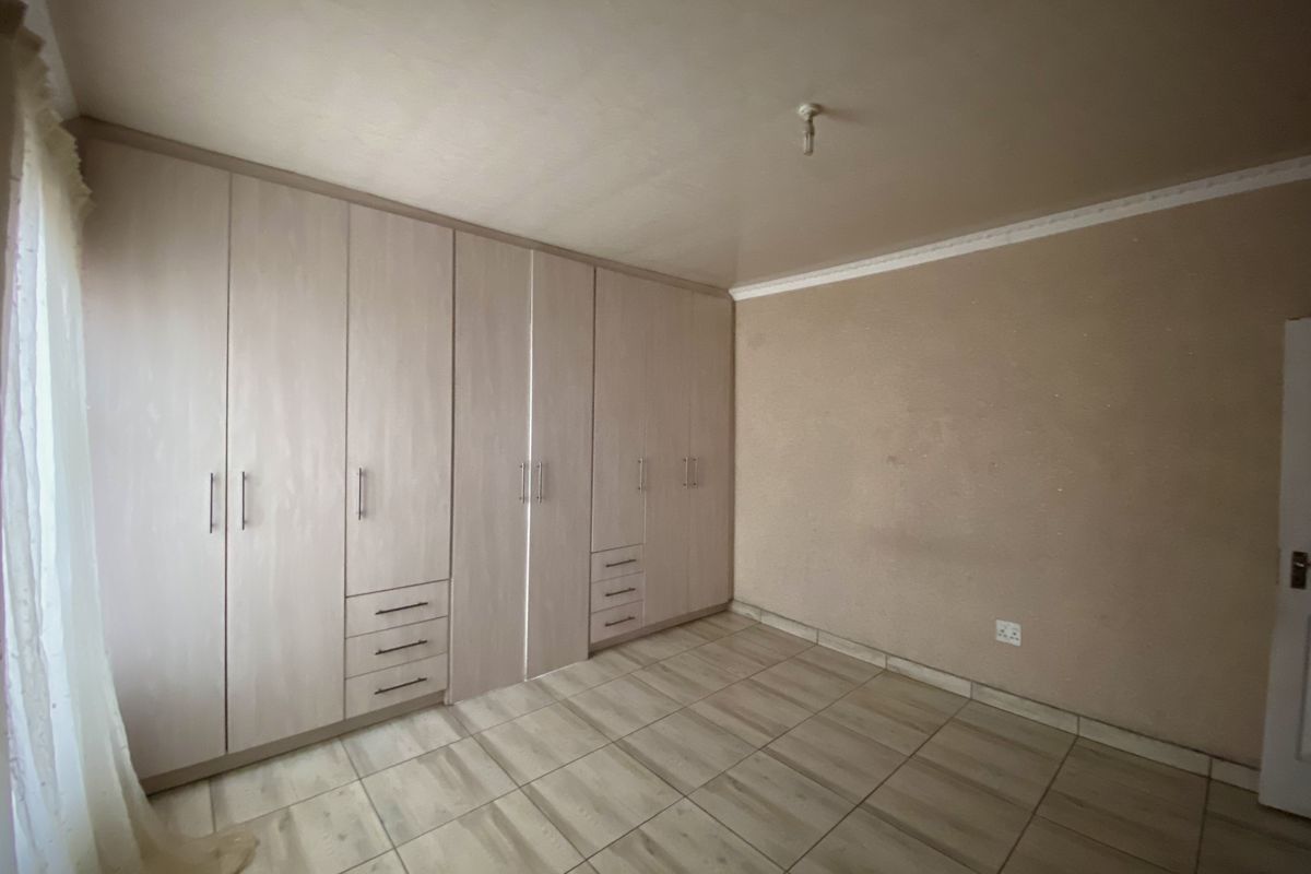 A spacious bedroom featuring neutral tiled flooring and extensive built-in wooden cupboards, offering ample storage space.