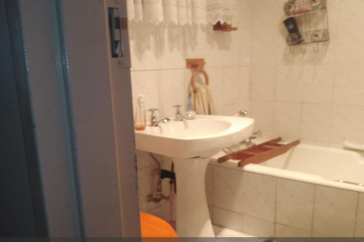 A dated bathroom featuring a pedestal sink and a standard bathtub with wall-mounted tiling.