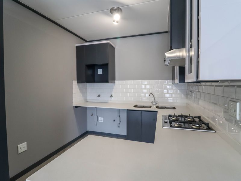A modern, clean kitchen featuring dark cabinetry, white subway tile backsplash, a gas hob, extractor fan, and a double sink with ample counter space.
