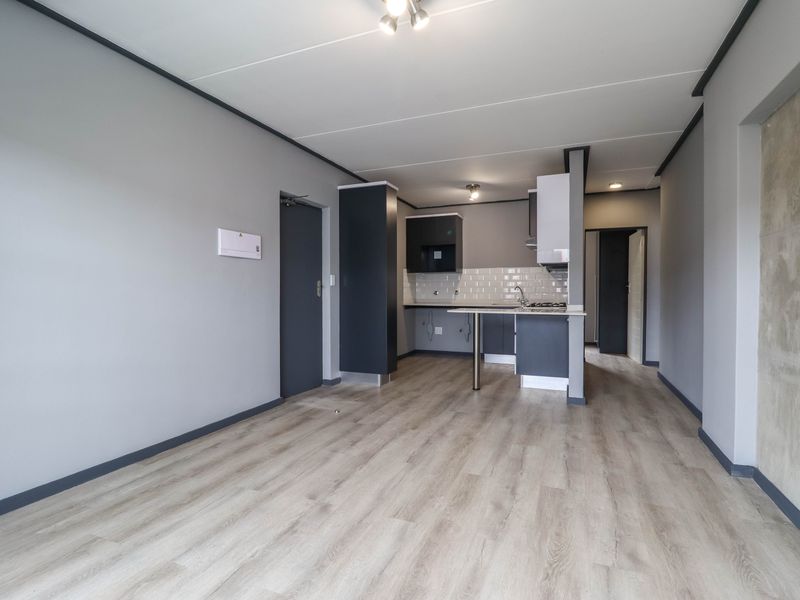 Modern open-plan living area featuring light laminate flooring and a contemporary kitchen with dark cabinetry, subway tile backsplash, and a breakfast bar.