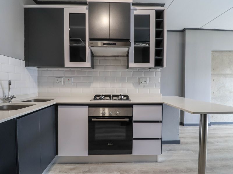 Modern kitchen featuring dark cabinetry, subway tile backsplash, integrated gas hob, built-in oven, and a functional breakfast bar with quartz countertops.