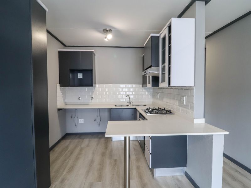 Modern kitchen featuring dark and white cabinetry, a gas hob, subway tile backsplash, and a breakfast bar with laminate flooring.