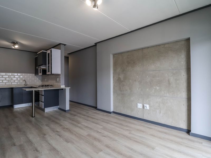 Modern open-plan living area featuring laminate flooring, a concrete feature wall, and a compact kitchen with built-in cabinetry and a gas hob.
