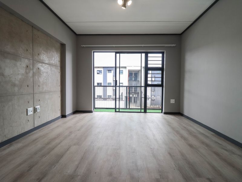 An empty living room featuring modern laminate flooring, a concrete feature wall, and a sliding glass door leading to a balcony.