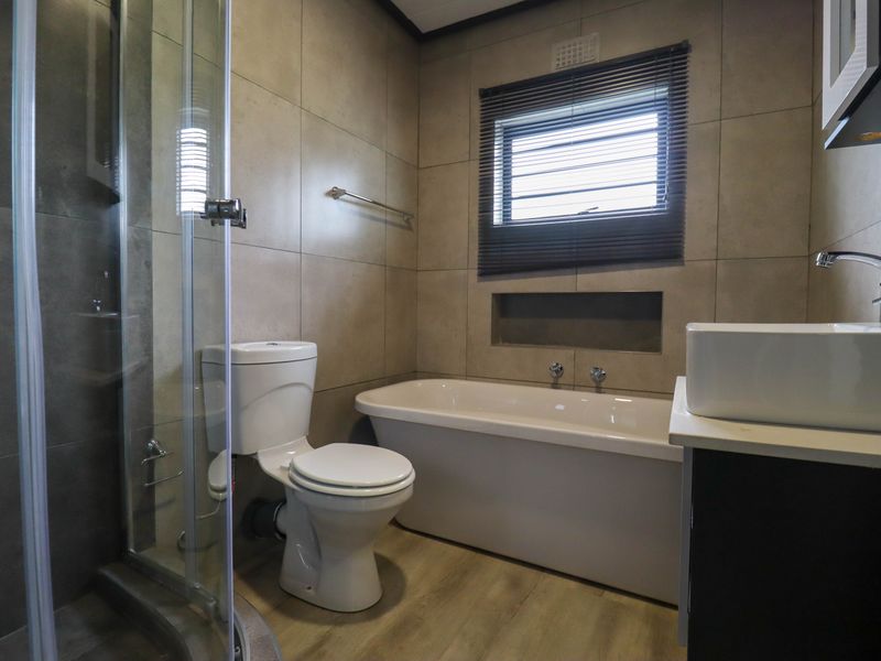 Modern bathroom featuring a glass shower enclosure, a bathtub, a vanity basin, and neutral wall tiling with a recessed storage niche.