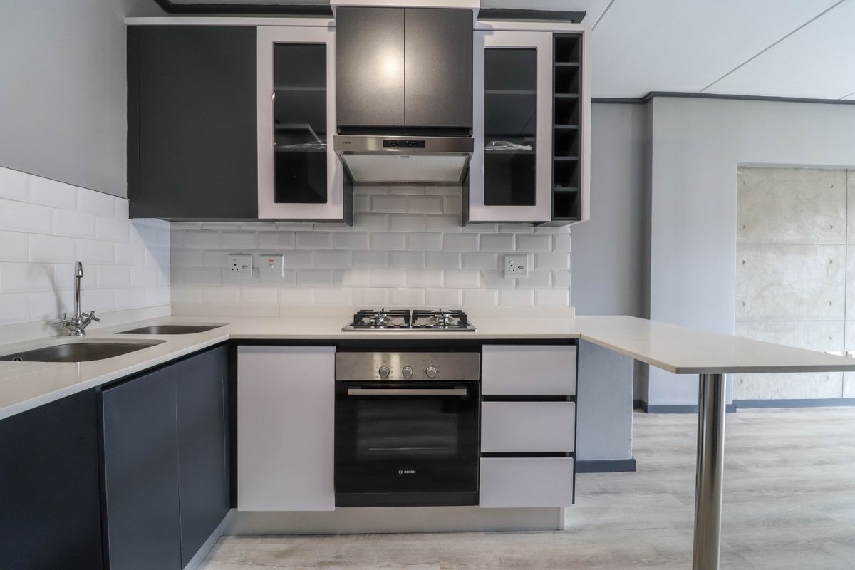 Modern kitchen featuring dark cabinetry, subway tile backsplash, integrated gas hob, built-in oven, and a functional breakfast bar with quartz countertops.