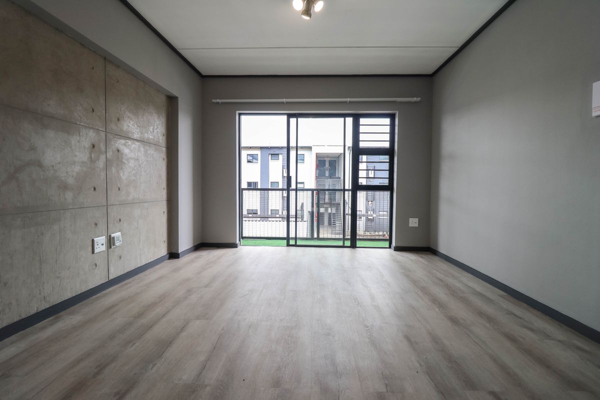 An empty living room featuring modern laminate flooring, a concrete feature wall, and a sliding glass door leading to a balcony.
