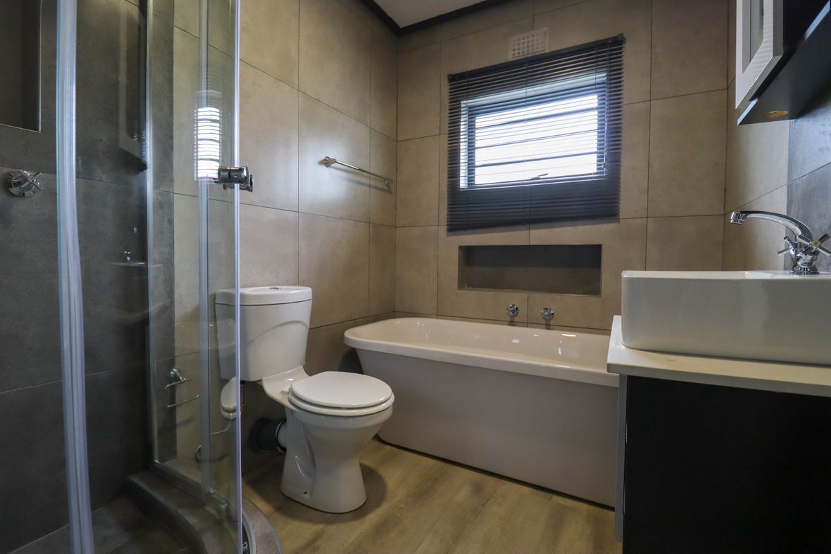 Modern bathroom featuring a glass shower enclosure, a bathtub, a vanity basin, and neutral wall tiling with a recessed storage niche.