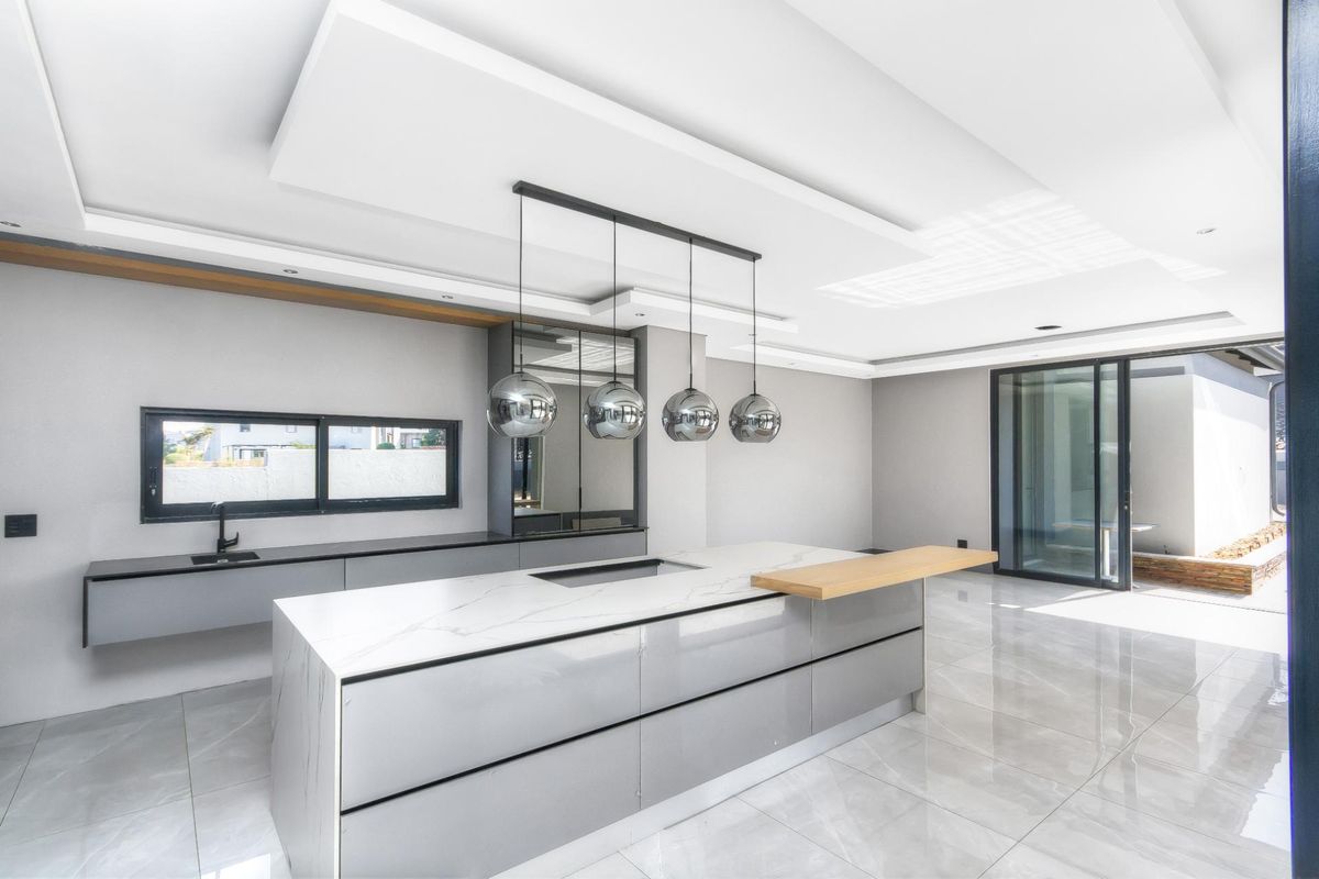 Modern kitchen featuring a large central island with stone countertop, integrated hob, sleek cabinetry, and large sliding glass doors leading to the patio.