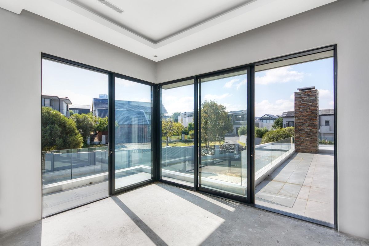 A bright, empty living space featuring expansive floor-to-ceiling glass sliding doors that open onto a tiled balcony with a stone-clad chimney feature.