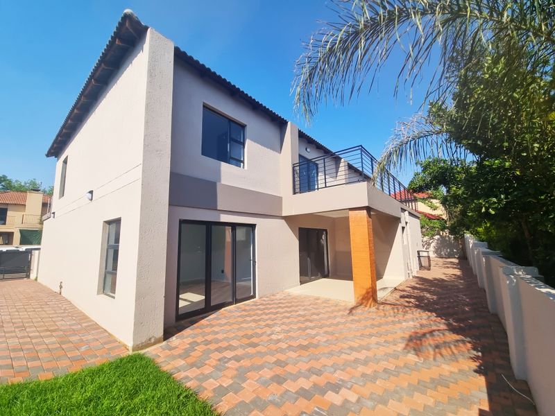 Rear view of a double-story house featuring a paved patio area, a balcony with metal railings, and large sliding glass doors.